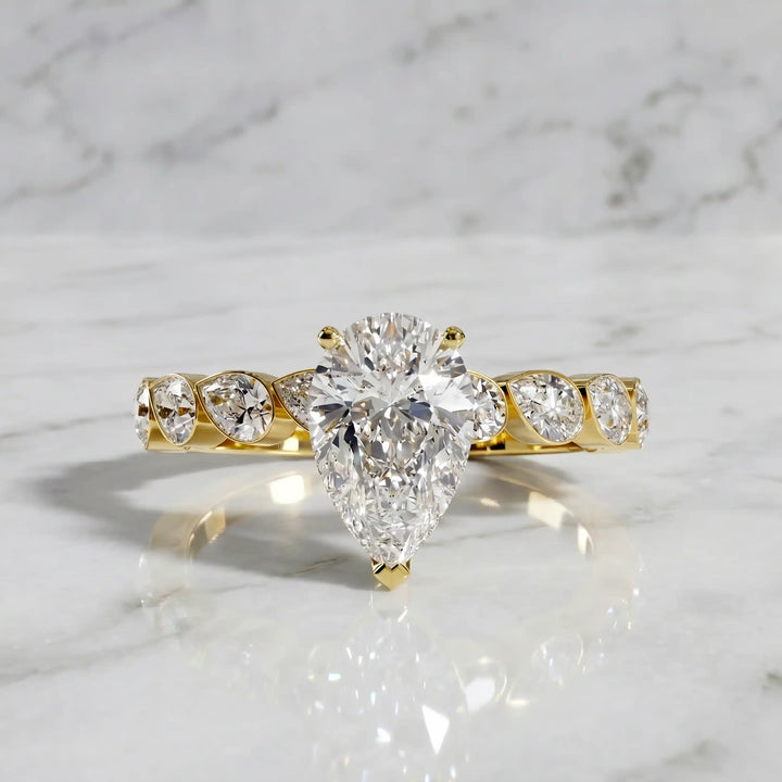 Pear lab-grown diamond engagement ring with bezel-set pear side stones displayed on surface.