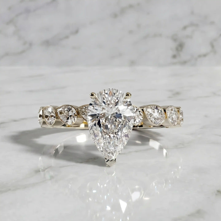 Pear lab-grown diamond engagement ring with bezel-set pear side stones displayed on surface.