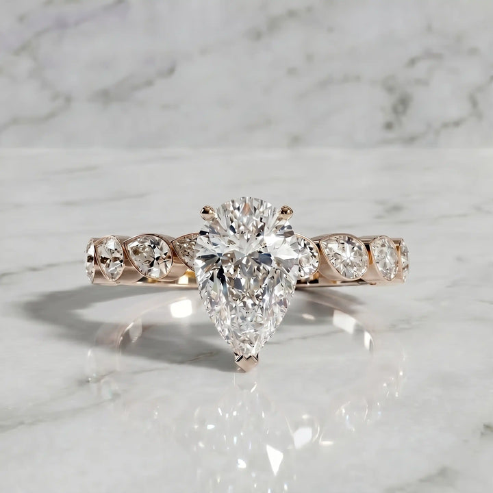 Pear lab-grown diamond engagement ring with bezel-set pear side stones displayed on surface.