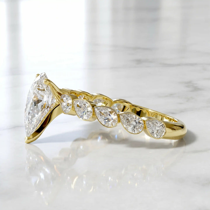 Pear lab-grown diamond engagement ring with bezel-set pear side stones displayed on surface.