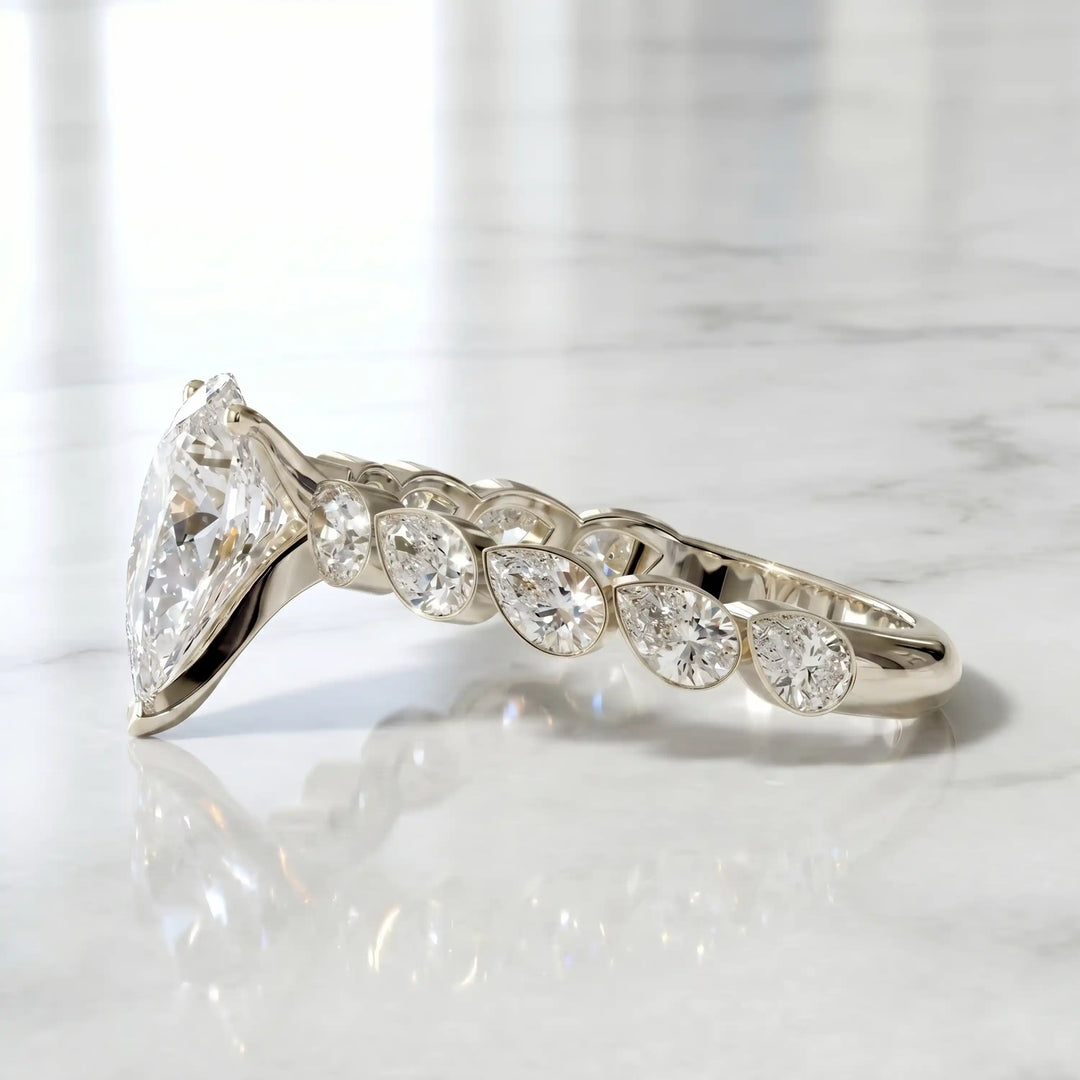 Pear lab-grown diamond engagement ring with bezel-set pear side stones displayed on surface.