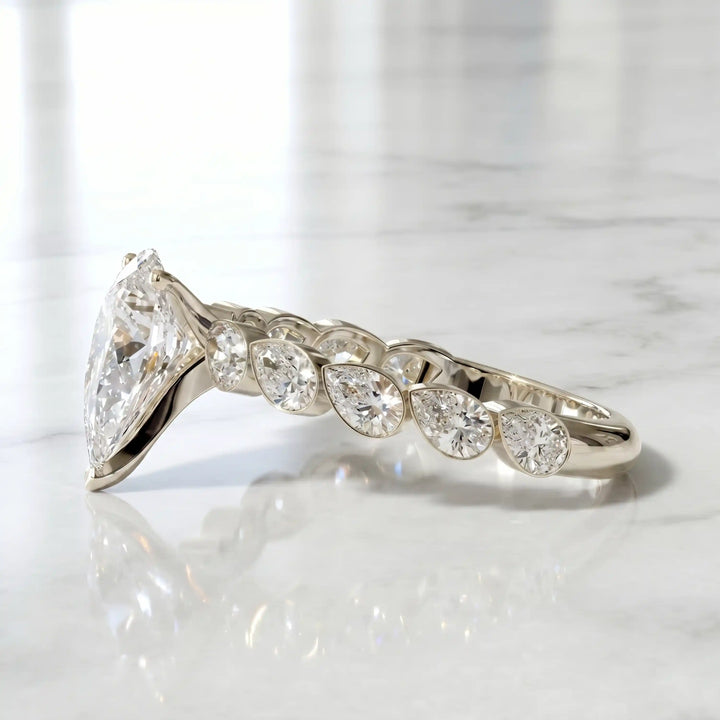 Pear lab-grown diamond engagement ring with bezel-set pear side stones displayed on surface.