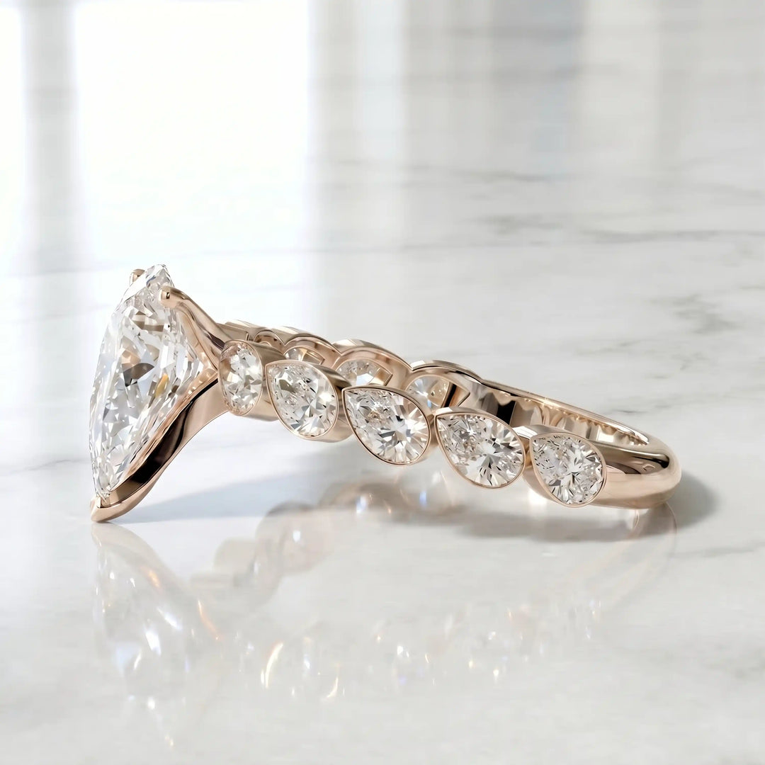 Pear lab-grown diamond engagement ring with bezel-set pear side stones displayed on surface.