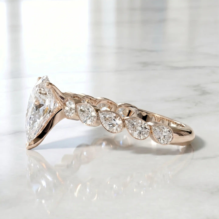 Pear lab-grown diamond engagement ring with bezel-set pear side stones displayed on surface.