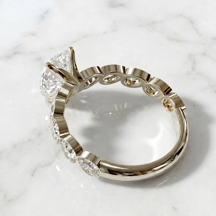Pear lab-grown diamond engagement ring with bezel-set pear side stones displayed on surface.