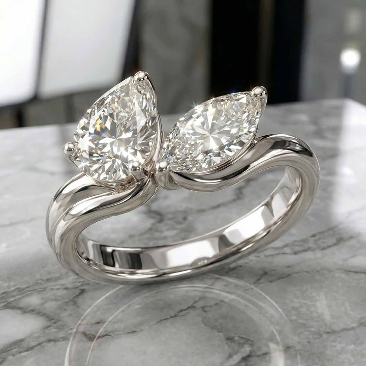 1.10 carat pear and marquise lab-grown diamond toi et moi engagement ring displayed on marble.
