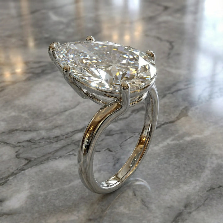 Pear-shaped lab-grown diamond cathedral solitaire engagement ring displayed on stone surface.
