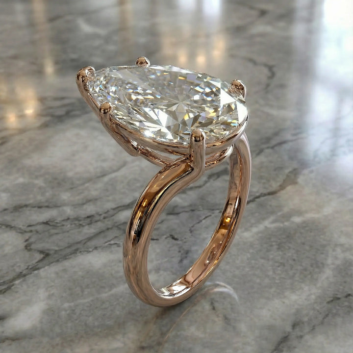 Pear-shaped lab-grown diamond cathedral solitaire engagement ring displayed on stone surface.
