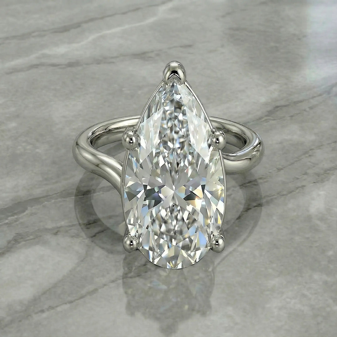 Pear-shaped lab-grown diamond cathedral solitaire engagement ring displayed on stone surface.
