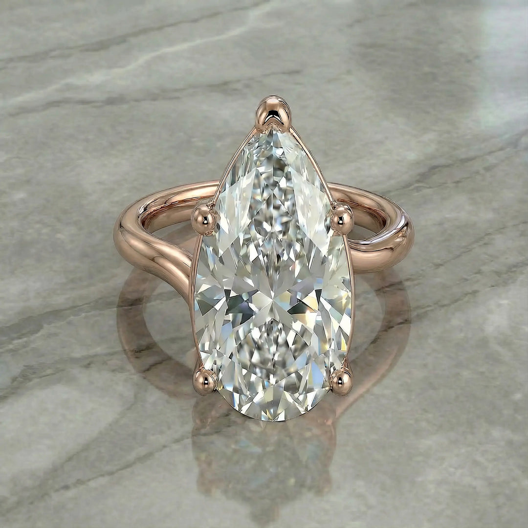 Pear-shaped lab-grown diamond cathedral solitaire engagement ring displayed on stone surface.
