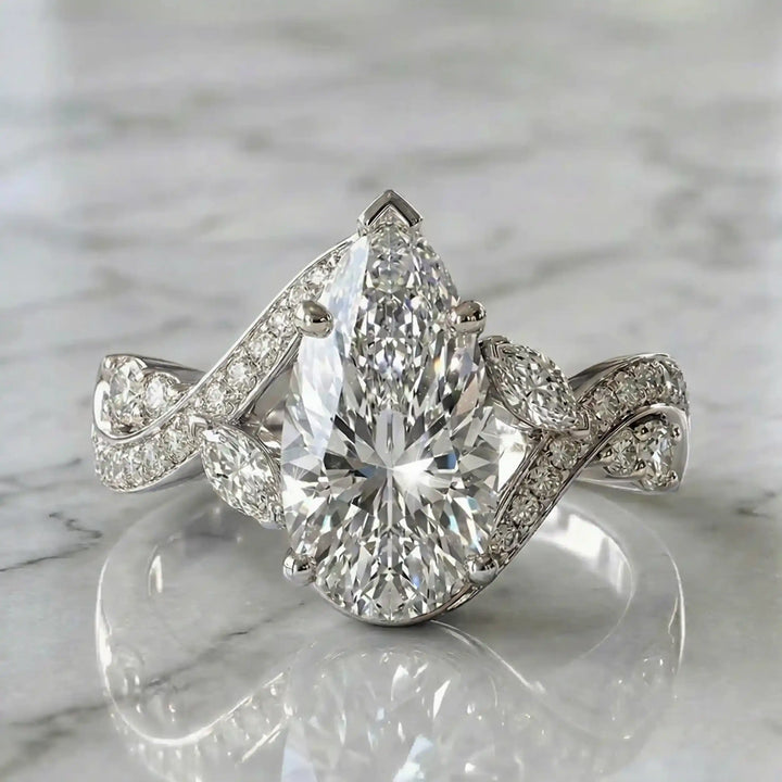 3 carat pear lab diamond twisted three-stone engagement ring displayed on marble surface.
