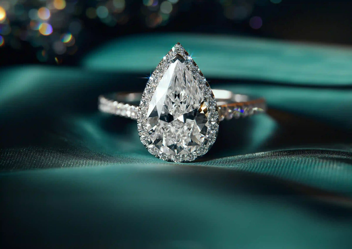 Pear-shaped diamond halo ring on teal fabric at RUDIX Jewellery