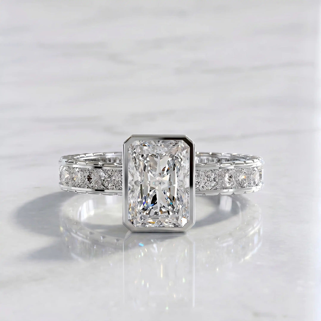Radiant lab-grown diamond engagement ring with princess cut channel set band on marble display.