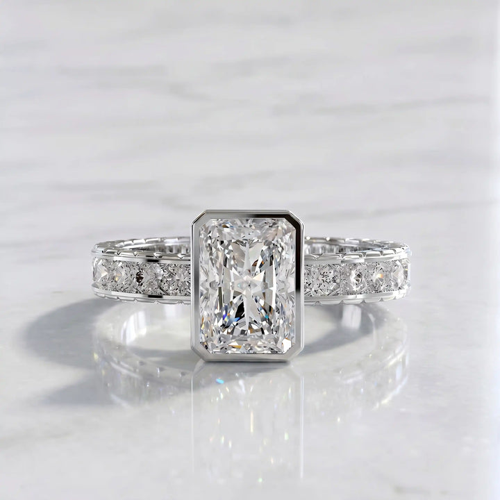 Radiant lab-grown diamond engagement ring with princess cut channel set band on marble display.