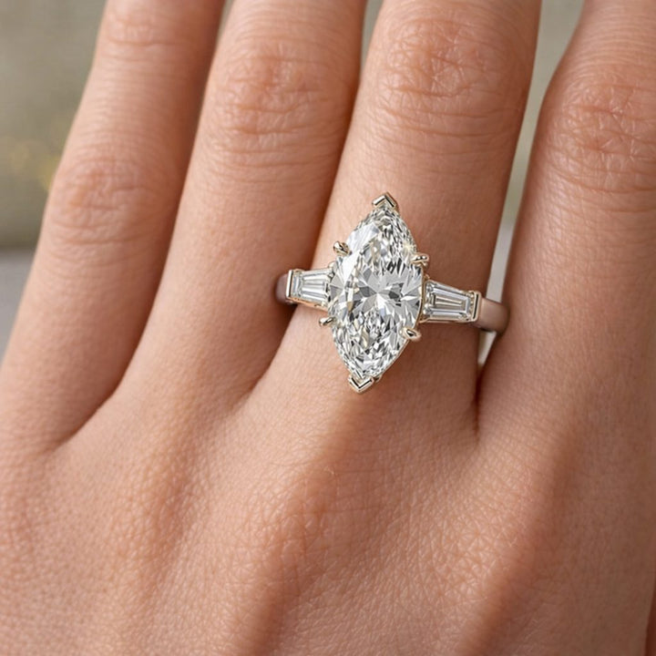 Three-stone marquise lab-grown diamond engagement ring displayed on marble surface.
