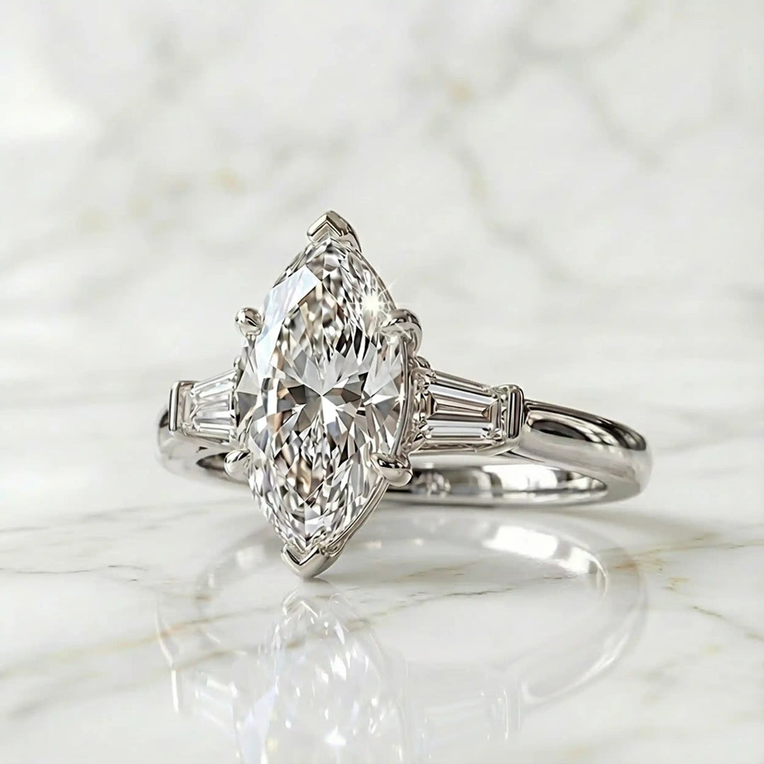 Three-stone marquise lab-grown diamond engagement ring displayed on marble surface.