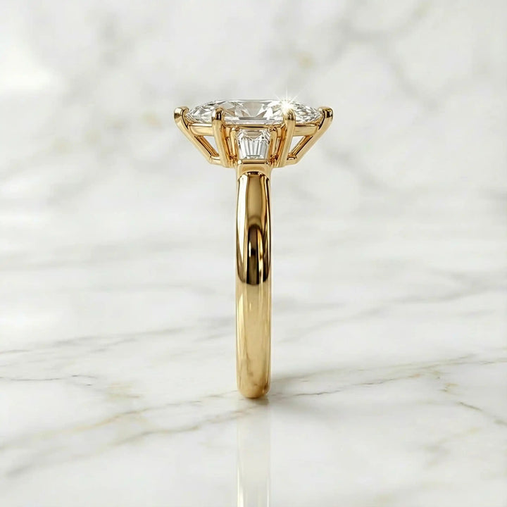 Three-stone marquise lab-grown diamond engagement ring displayed on marble surface.