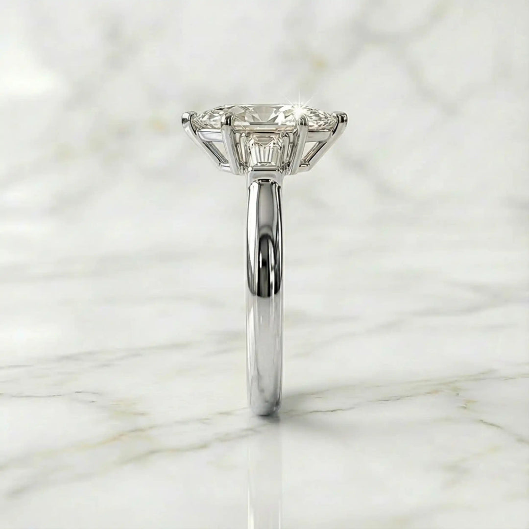 Three-stone marquise lab-grown diamond engagement ring displayed on marble surface.