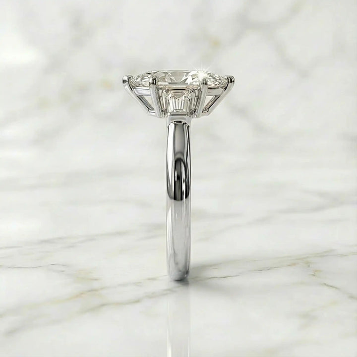 Three-stone marquise lab-grown diamond engagement ring displayed on marble surface.