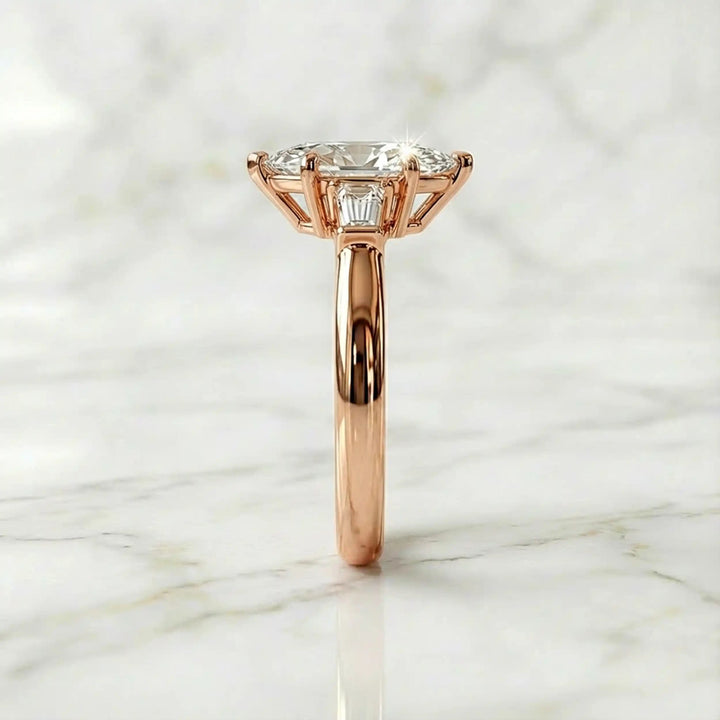Three-stone marquise lab-grown diamond engagement ring displayed on marble surface.