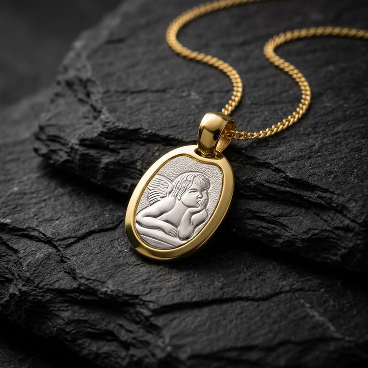 Two-tone gold oval angel medal pendant with a raised white gold Raphael cherub in relief in a polished yellow gold frame, 18.6 x 14 mm, on a yellow gold chain resting on dark slate stone