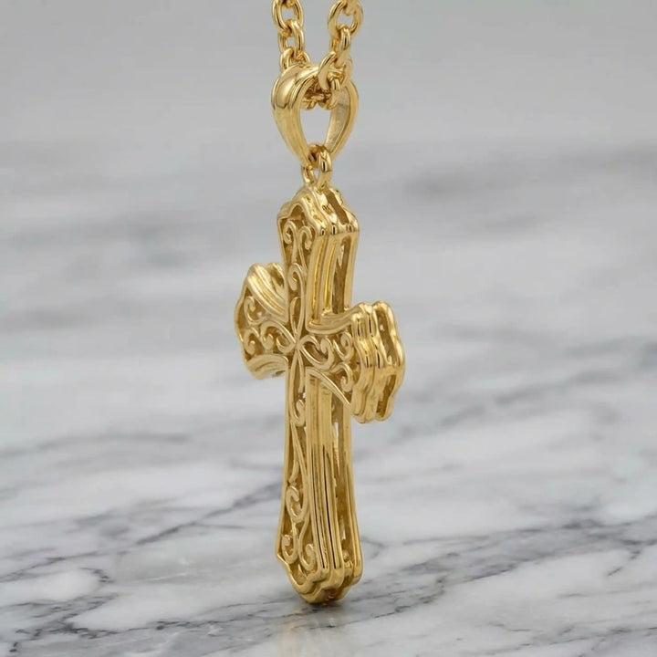 Victorian hollow cross pendant with intricate scrollwork displayed on chain over marble background.