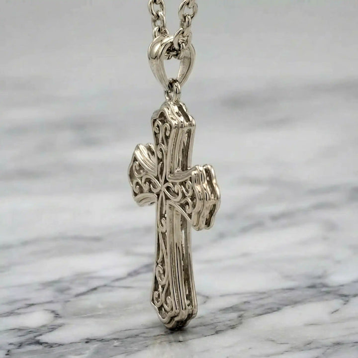 Victorian hollow cross pendant with intricate scrollwork displayed on chain over marble background.