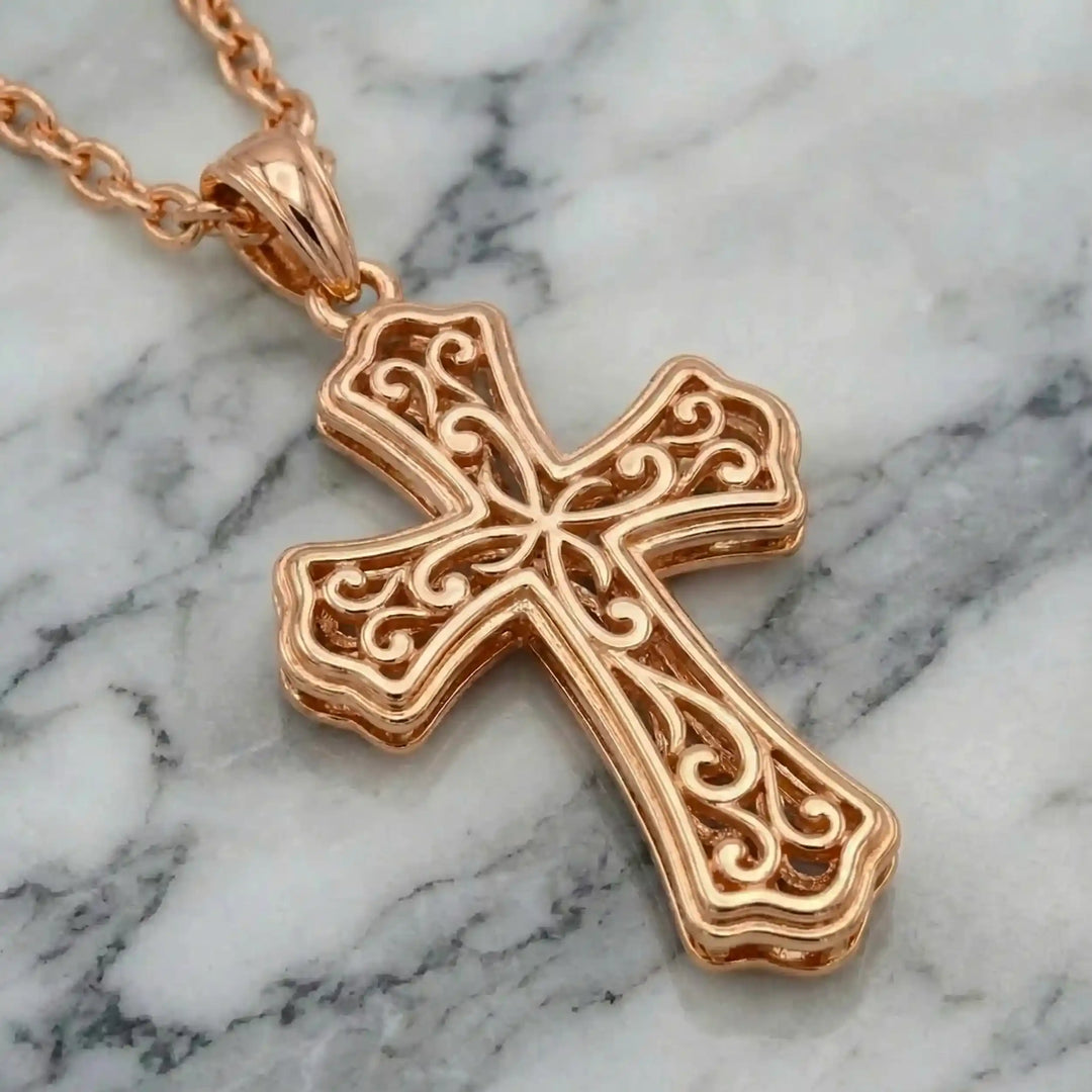 Victorian hollow cross pendant with intricate scrollwork displayed on chain over marble background.