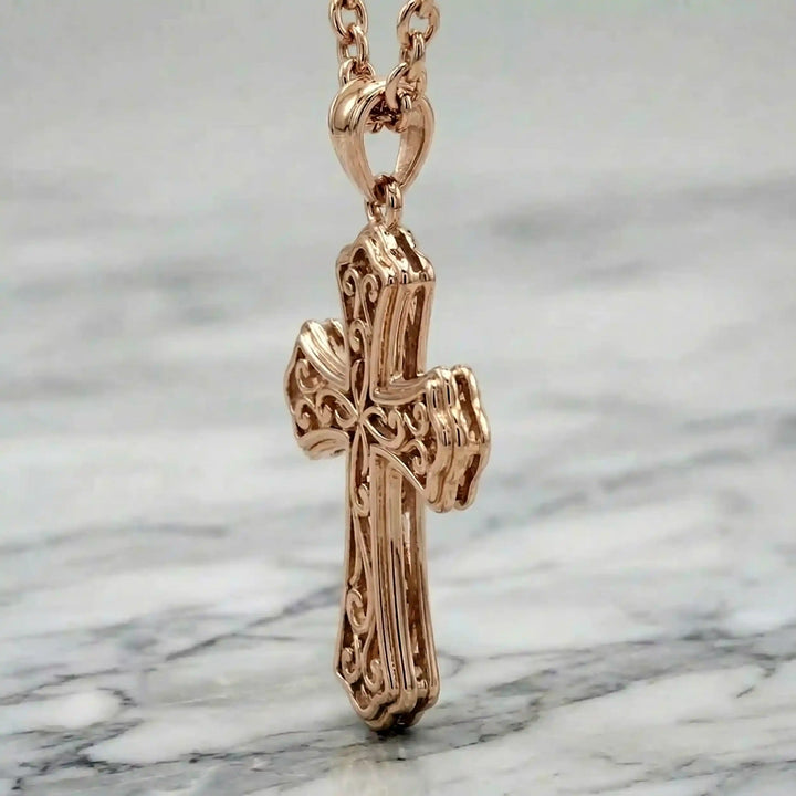 Victorian hollow cross pendant with intricate scrollwork displayed on chain over marble background.