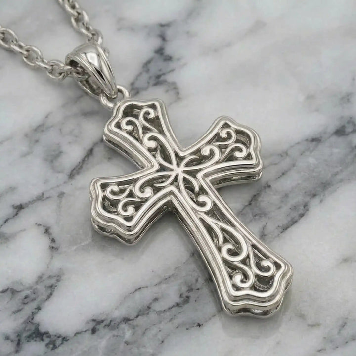 Victorian hollow cross pendant with intricate scrollwork displayed on chain over marble background.
