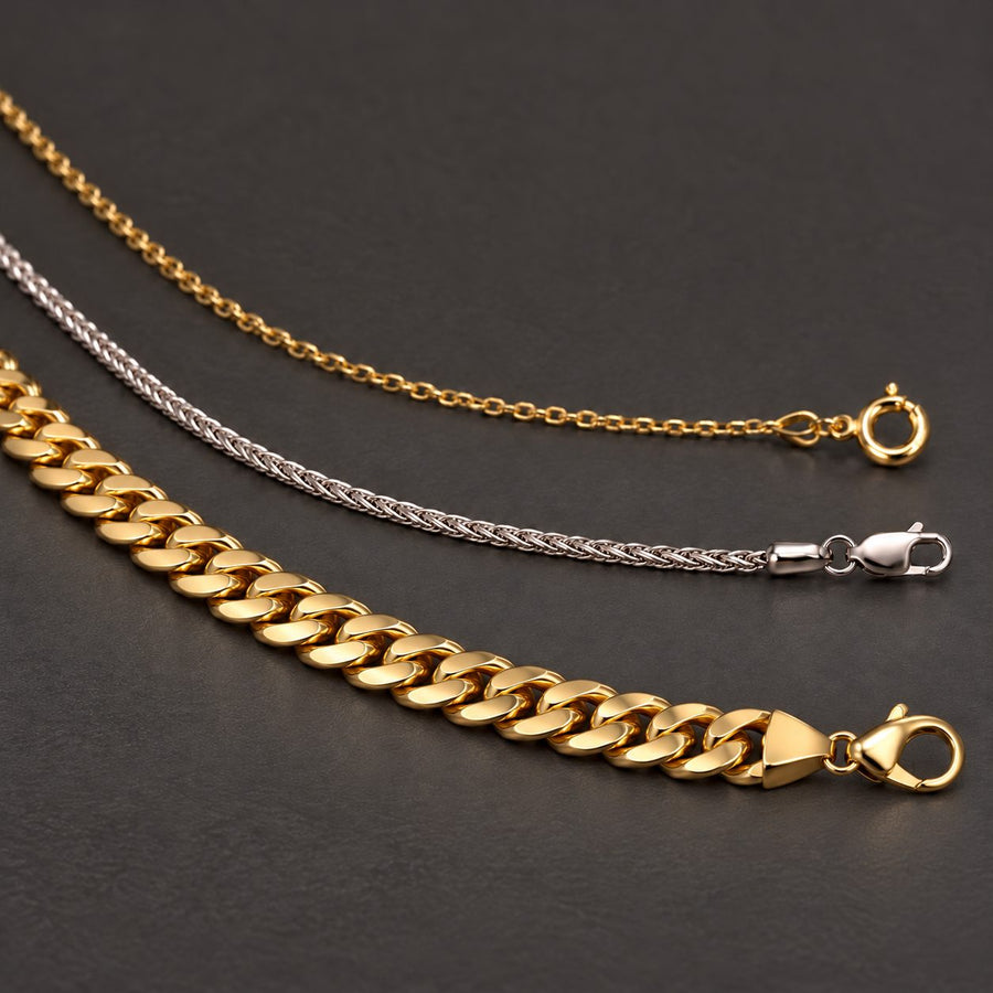 Yellow gold Cuban link, white gold wheat, and yellow gold cable chains on charcoal — solid gold chain essentials at Rudix Jewellery