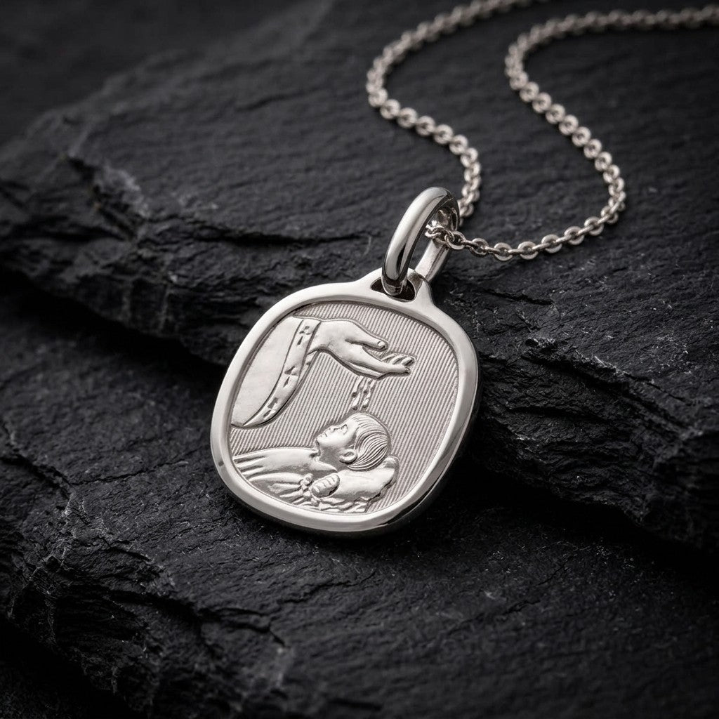 White gold cushion square baptism medal pendant with a polished rim, ribbed background and a raised hand pouring water over a sleeping infant beside a priest's stole with crosses, 15 mm wide, on a white gold chain resting on dark slate stone