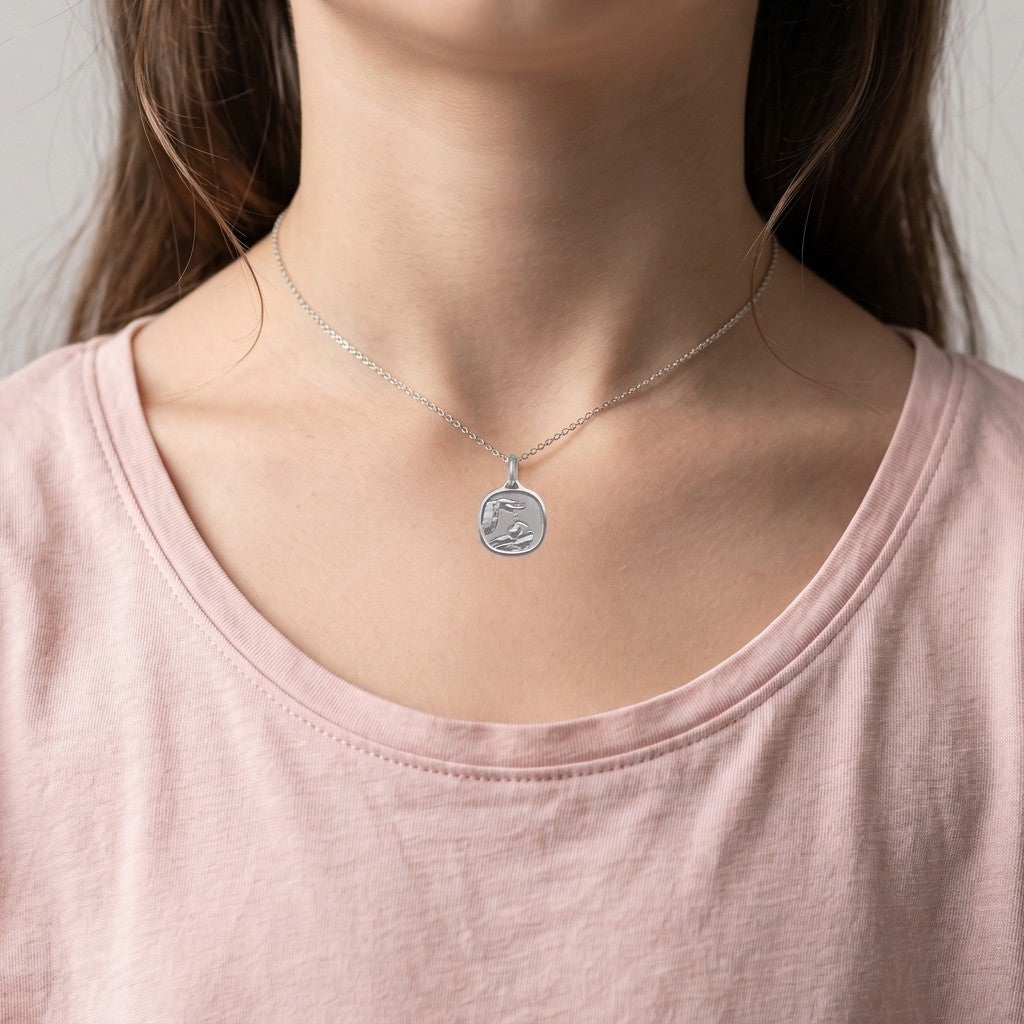 White gold cushion square baptism medal pendant with a polished rim, ribbed background and a raised hand pouring water over a sleeping infant beside a priest's stole with crosses, 15 mm wide, worn by a girl on a fine white gold chain