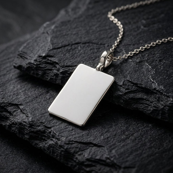 White gold plain rectangular tag pendant, 23 x 16 mm, 0.5 mm thick, on a white gold chain resting on dark slate stone