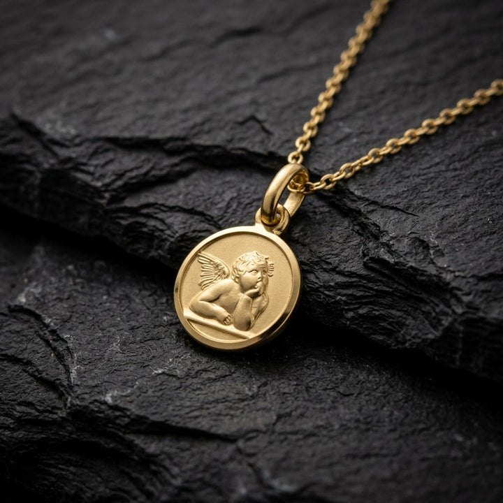 Yellow gold round angel medal pendant with a raised Raphael cherub in relief, 8 mm, on a yellow gold chain resting on dark slate stone