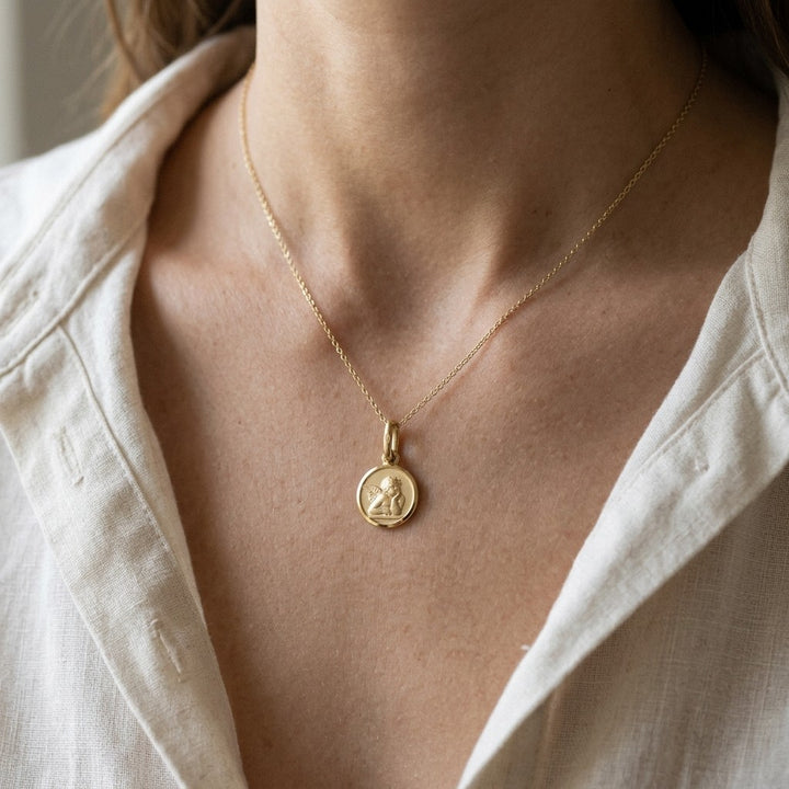 Yellow gold round angel medal pendant with a raised Raphael cherub in relief, 10 mm, worn by a boy on a fine yellow gold chain