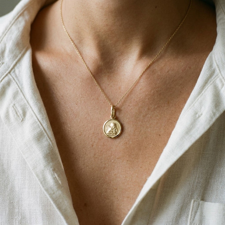 Yellow gold round angel medal pendant with a raised Raphael cherub in relief, 10 mm, worn by a girl on a fine yellow gold chain
