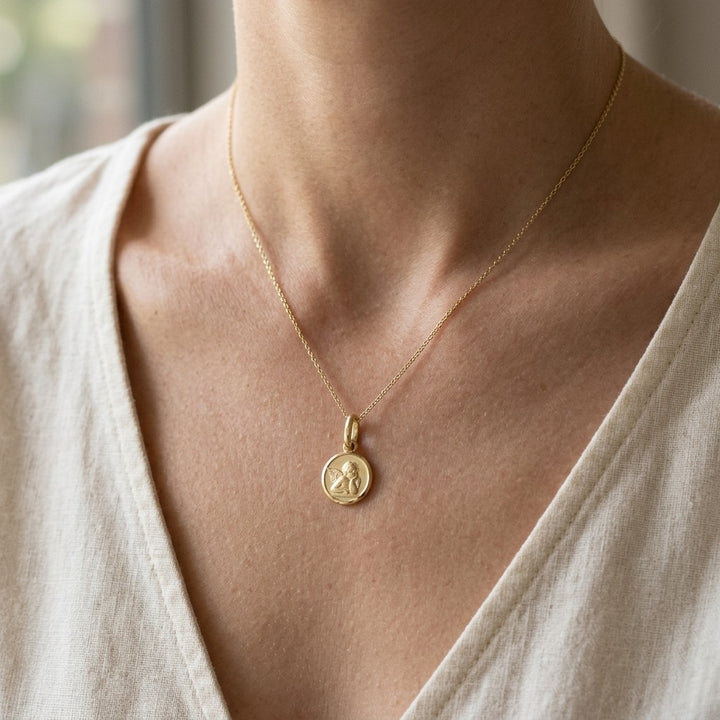 Yellow gold round angel medal pendant with a raised Raphael cherub in relief, 12 mm, worn by a girl on a fine yellow gold chain