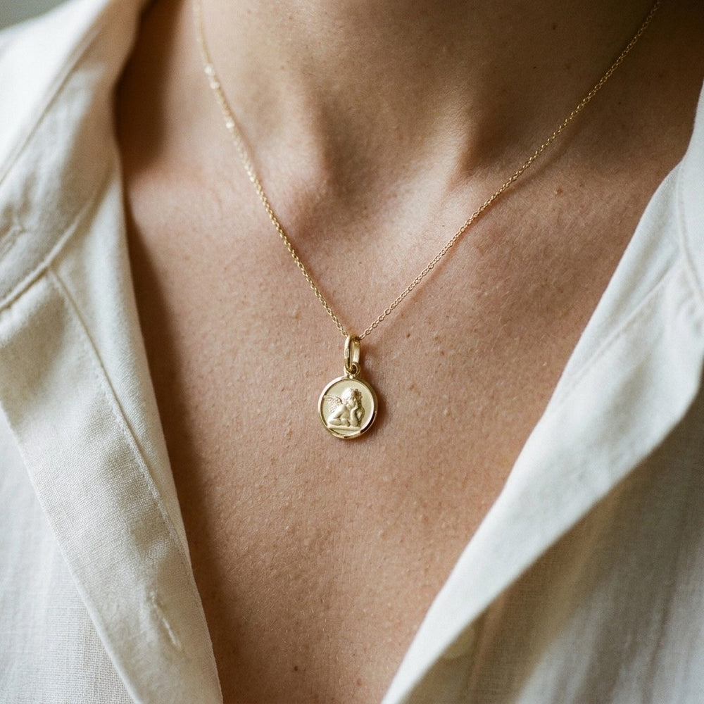 Yellow gold round angel medal pendant with a raised Raphael cherub in relief, 12 mm, worn by a man on a fine yellow gold chain