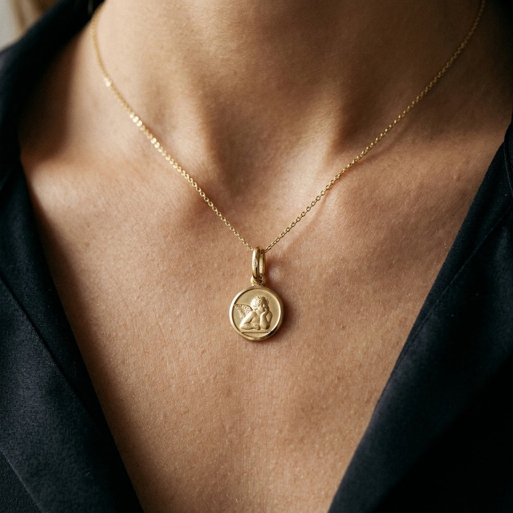 Yellow gold round angel medal pendant with a raised Raphael cherub in relief, 14 mm, worn by a man on a fine yellow gold chain