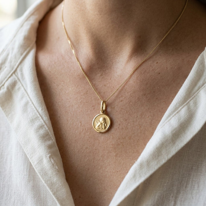 Yellow gold round angel medal pendant with a raised Raphael cherub in relief, 16 mm, worn by a boy on a fine yellow gold chain