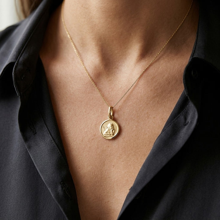 Yellow gold round angel medal pendant with a raised Raphael cherub in relief, 16 mm, worn by a man on a fine yellow gold chain