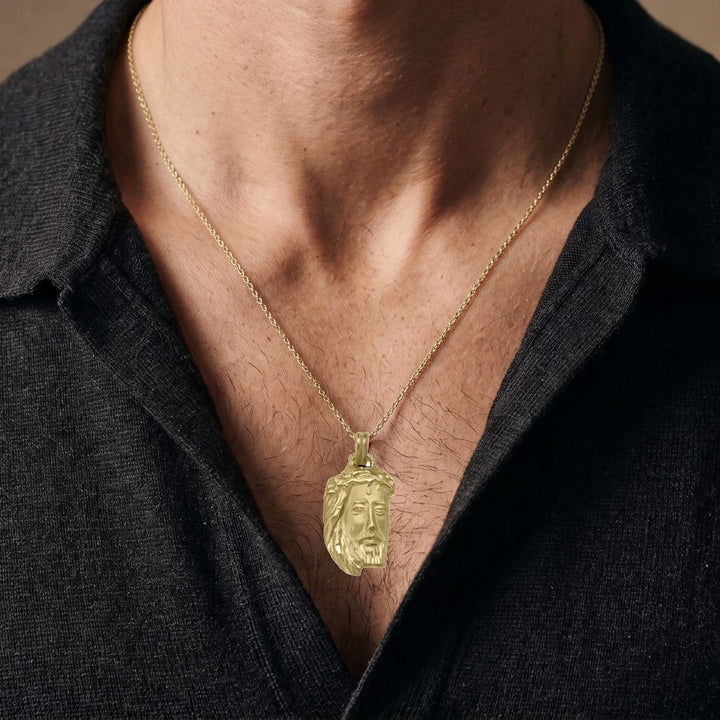 Yellow gold Jesus head pendant with a crown of thorns, flowing hair and a diamond-cut beard, 21.5 mm wide and 33.1 mm tall, worn by a man on a fine yellow gold chain