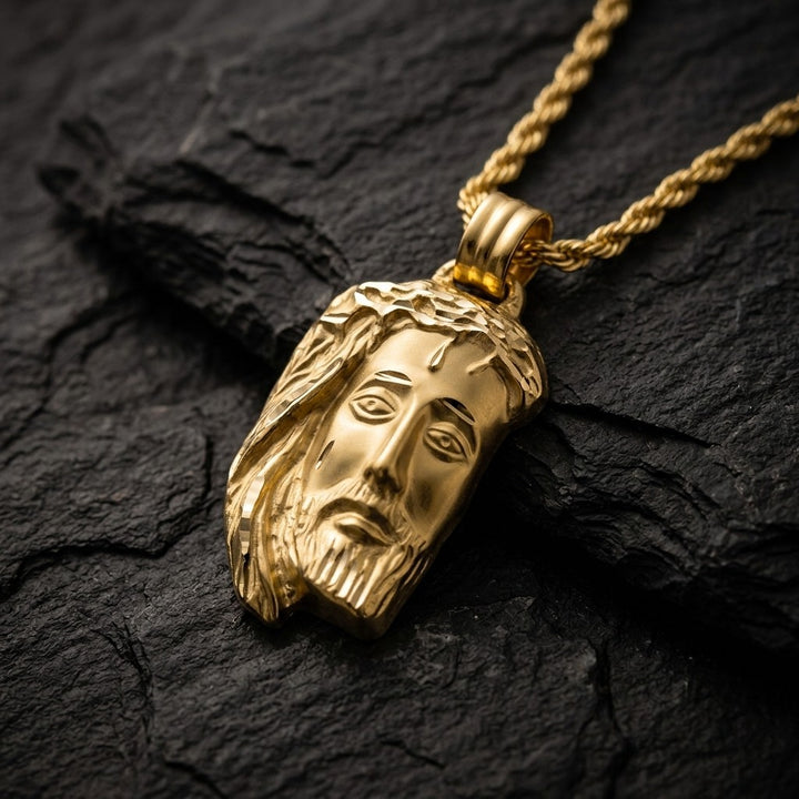 Yellow gold Jesus head pendant with a crown of thorns, flowing hair and a diamond-cut beard, 25.8 mm wide and 39.4 mm tall, on a yellow gold chain resting on dark slate stone