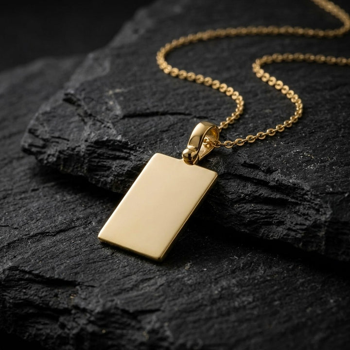 Yellow gold plain rectangular tag pendant, 19 x 13 mm, 0.5 mm thick, on a yellow gold chain resting on dark slate stone