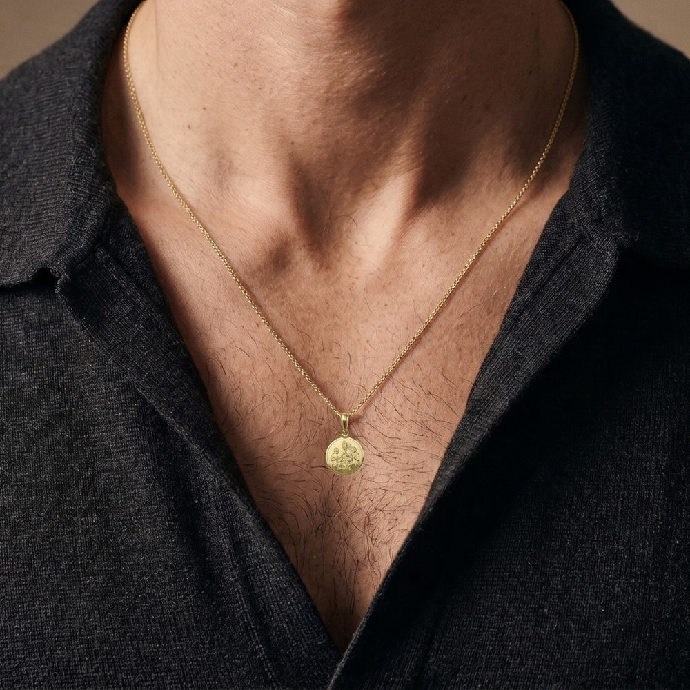 Yellow gold round confirmation medal pendant with a bishop in a tall mitre laying his hand on two kneeling children, standing children at each side and a polished rim, 12 mm wide, worn by a man on a fine yellow gold chain