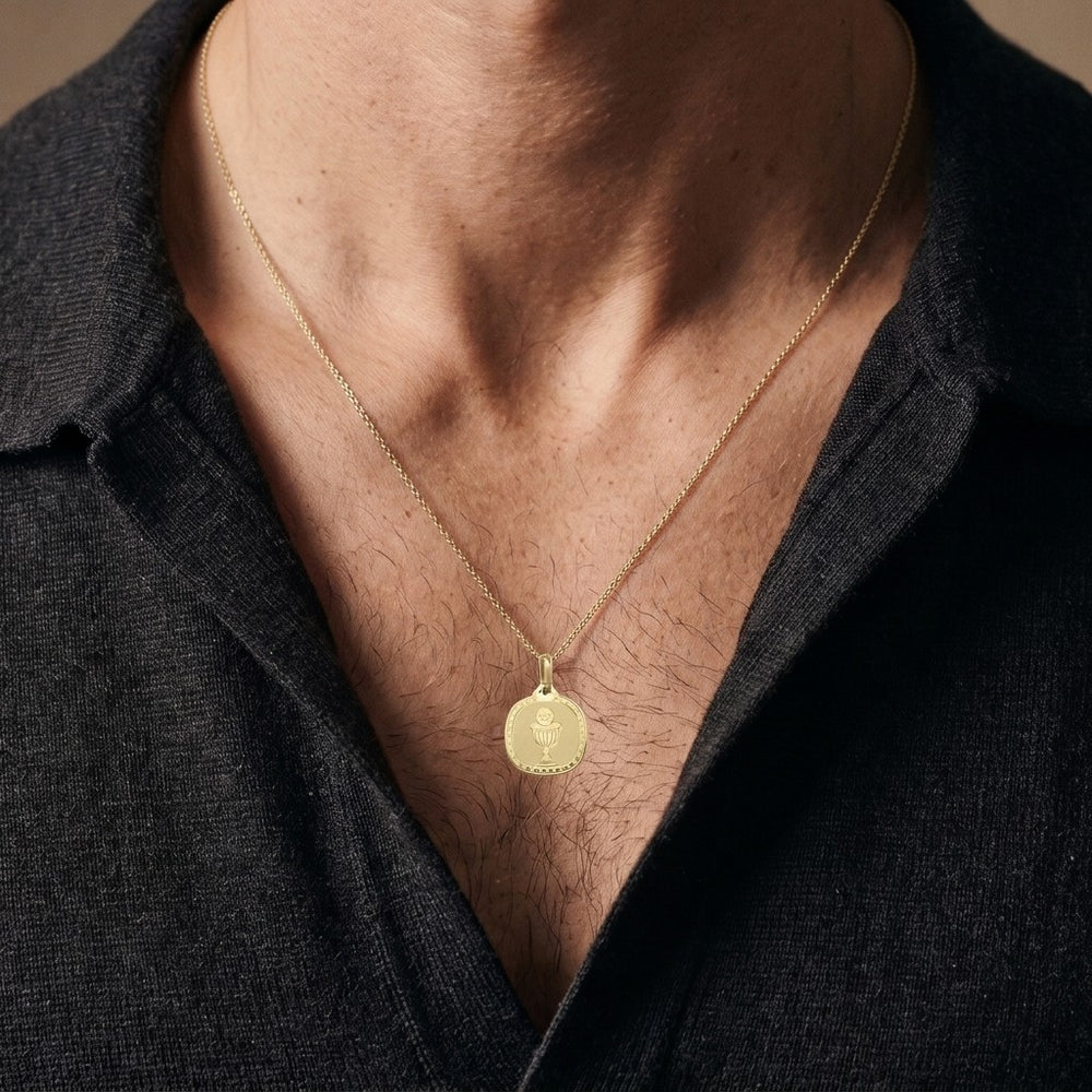 Yellow gold rounded square communion medal pendant with an engraved chalice and host inside a clover-patterned border, 16.2 mm wide, worn by a man on a fine yellow gold chain