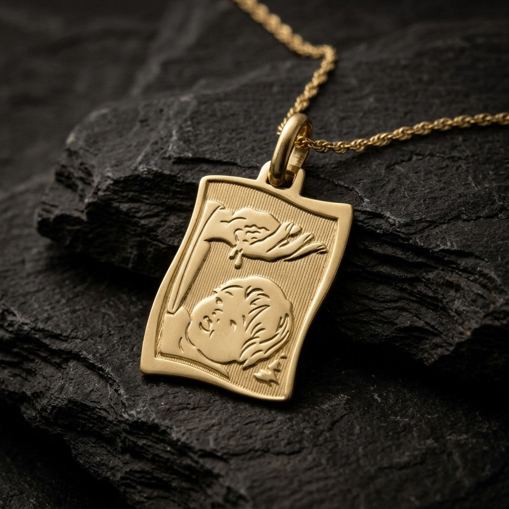 Yellow gold wavy rectangle scroll-style baptism medal pendant with a ribbed background and a raised hand pouring water over an infant's face, 15 mm wide, on a yellow gold chain resting on dark slate stone